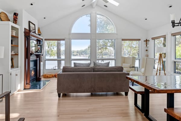 A cozy living room featuring a sofa, fireplace, and large windows overlooking a lake.