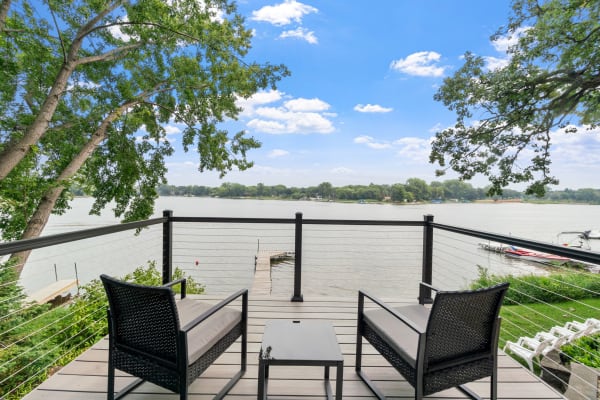 A balcony overlooking a serene lake with chairs and a small table.