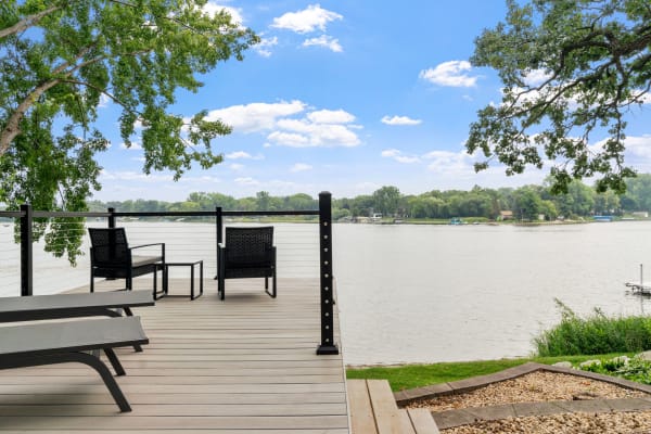 Lakeside deck with black chairs overlooking a calm lake and greenery.