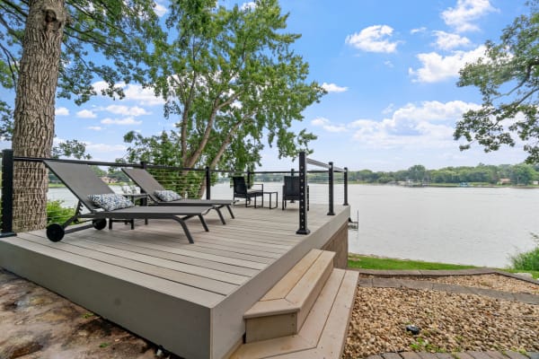 A wooden deck by the lake featuring lounge chairs and lush greenery.