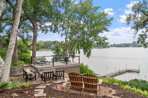 Outdoor seating area by a lake with Adirondack chairs and a dock in the background.