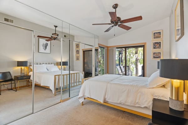 Modern bedroom featuring a made bed, mirrors, and a balcony view.