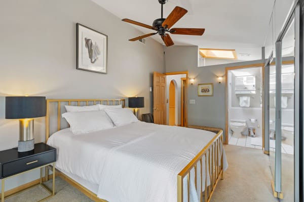 A modern bedroom with a gold bed frame, two lamps, and an en-suite bathroom visible.