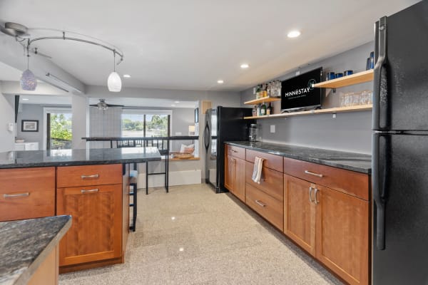 Contemporary kitchen with dark granite countertops and wooden cabinetry, featuring shelves of glassware.