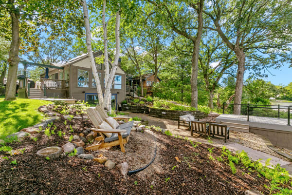 A cozy patio with lounge chairs surrounded by trees and landscaping, in front of a home.