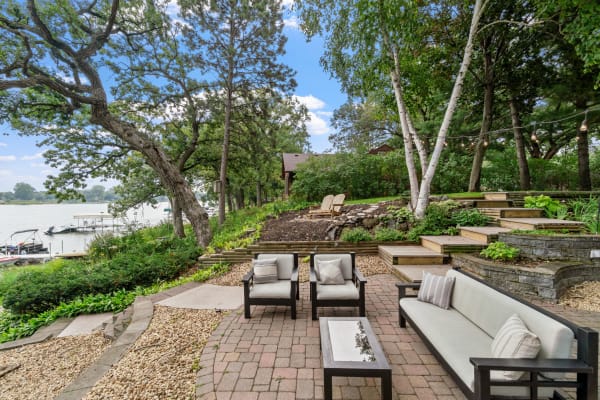 Lakeside outdoor living area with seating and lush greenery.
