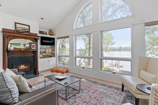 Living room with fireplace overlooking a lake through large arched windows.