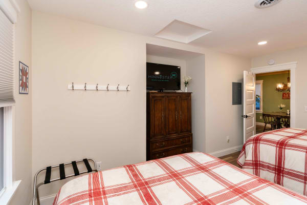 A cozy bedroom with two beds, a vintage armoire, and a TV mounted on the wall.