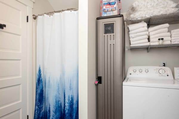 Laundry area featuring a blue-themed shower curtain, a gray locker, and a white washing machine with neatly stacked towels.