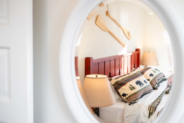 A rustic bedroom featuring a red bed frame, nature-themed pillows, and wooden oars on the wall, seen through a mirror.