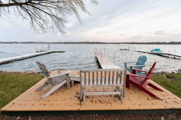 A tranquil lakeside view featuring colorful Adirondack chairs on a wooden deck.