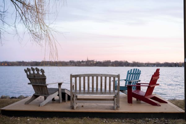A lakeside patio with colorful chairs and a bench at sunset