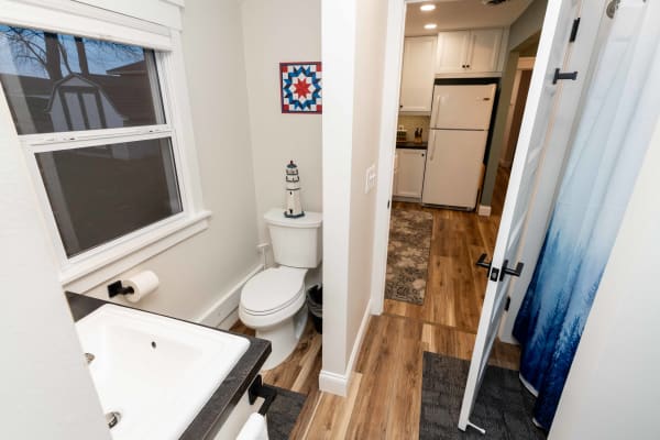 A view of a modern bathroom with a white toilet, sink, and a doorway to a kitchen.