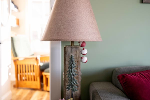 A rustic lamp with a tree carving and a beige lampshade in a living room.