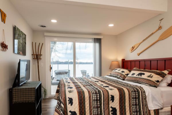 A rustic bedroom featuring a bear-patterned quilt, TV, and sliding glass door with a view of a lake.