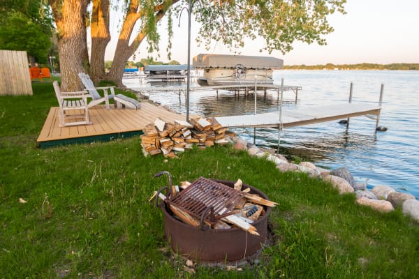 Wooden deck and fire pit by a calm lake with boats docked.