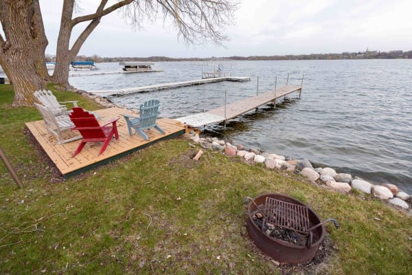Adirondack chairs by the lakeside with docks and a grill.