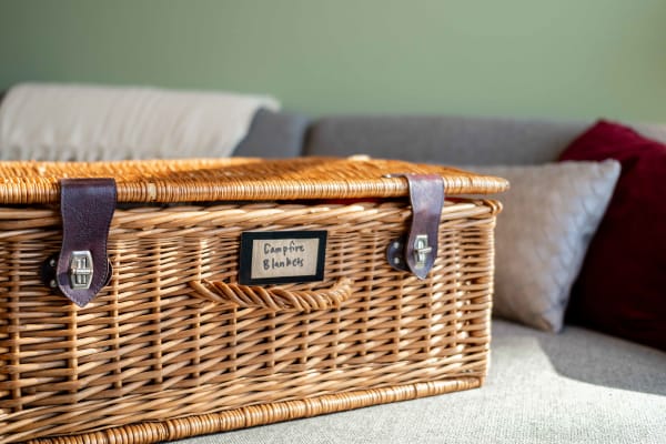 Wicker basket labeled 'Campfire Blankets' resting on a gray sofa with decorative pillows in the background.