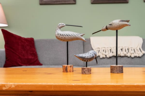 Three wooden bird sculptures on a table, with a cozy couch in the background.
