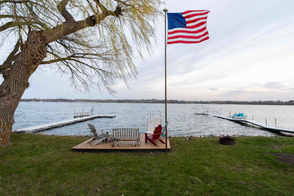 Lakeside view with an American flag, deck, and Adirondack chairs.