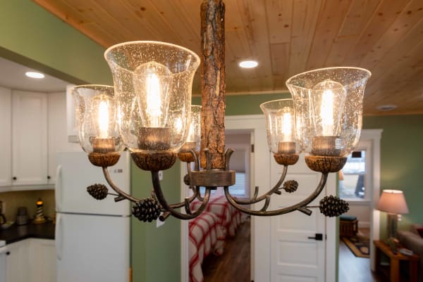 Close-up of a rustic chandelier with glass shades and pine cone details in a warm, inviting room.