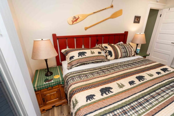 Interior view of a rustic-themed bedroom featuring bear-patterned bedding and a canoe paddle on the wall.