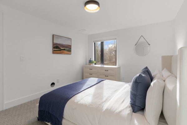 Modern bedroom with a king-sized bed, navy throw blanket, and a wooden dresser by the window.