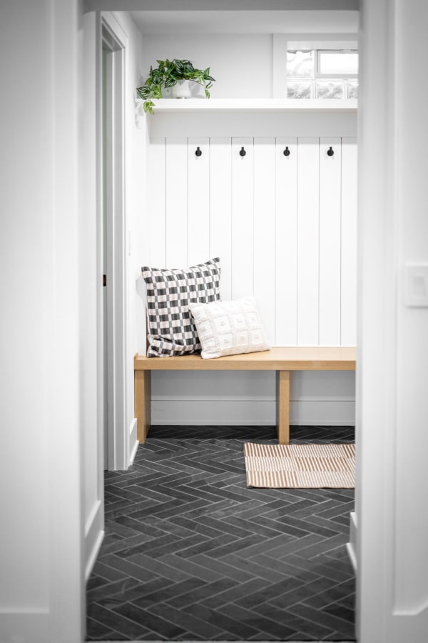 Minimalist entryway featuring a wooden bench with pillows and plants.