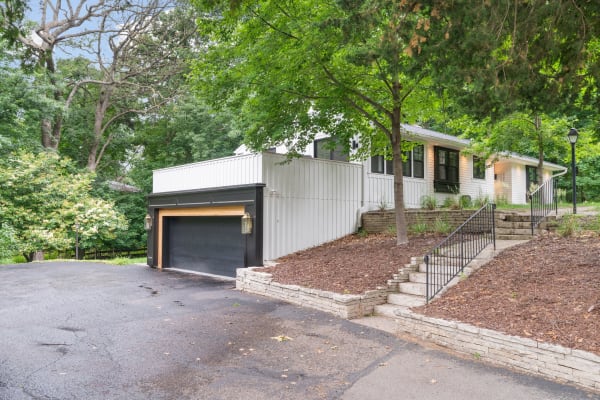Modern house with garage and stone steps, surrounded by trees and greenery.