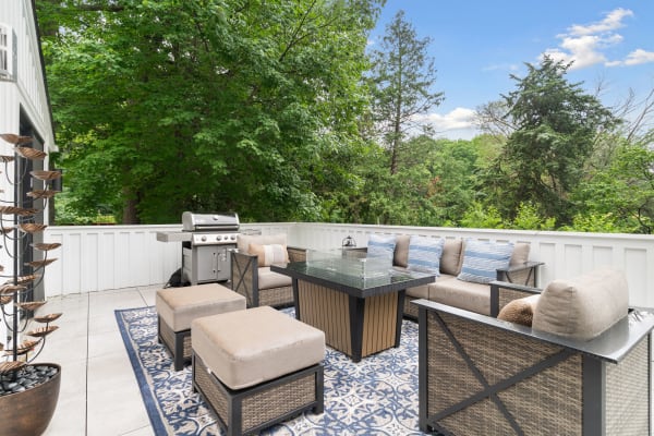 A modern outdoor patio featuring wicker furniture, a grill, and surrounding greenery.