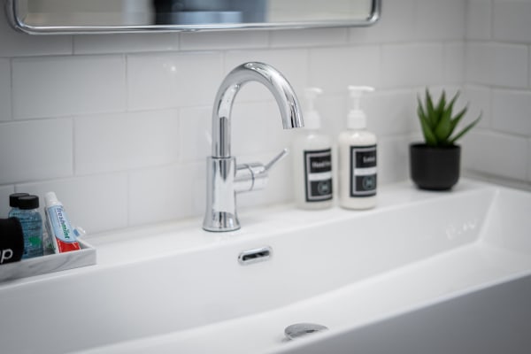 A modern sink with a chrome faucet, white tiles, and neatly arranged toiletries.