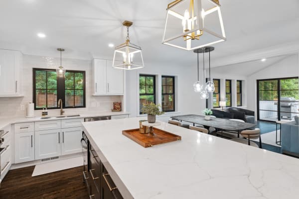 Bright and modern kitchen with white marble countertops and dark cabinetry, showcasing an inviting dining and living space.