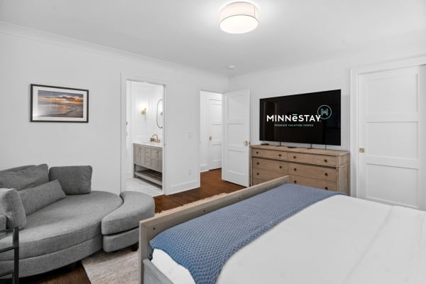 A modern bedroom featuring a bed, gray sectional couch, and a view of a bathroom.