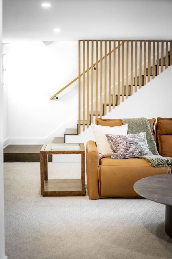 Modern living room with a brown leather sofa, side table, and a wooden staircase.