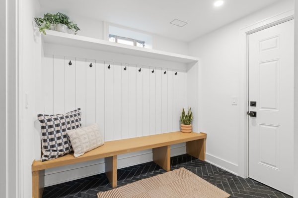 Minimalist entryway with a wooden bench, pillows, hooks, and plants.