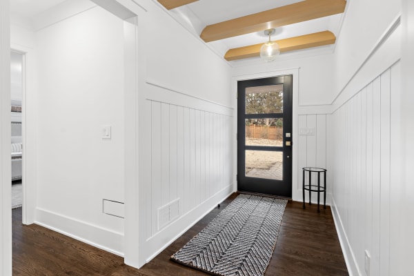 Modern hallway with white paneling, wooden beams, and a black door leading outside.