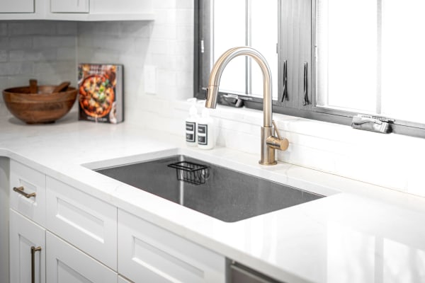 A modern kitchen featuring a dark sink, brass faucet, and wooden bowl next to a cookbook.