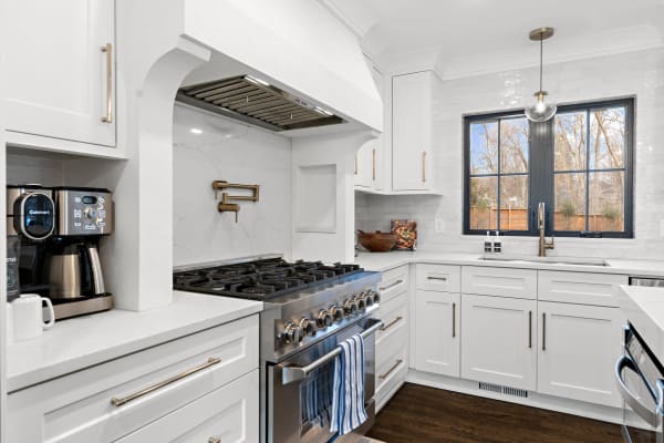 Modern kitchen featuring white cabinets, stainless steel stove, and a large window.