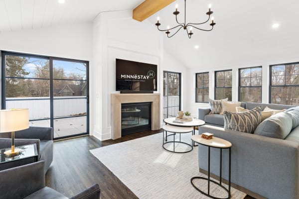Stylish living room with large windows, gray sofa, stylish chandelier, and modern coffee tables.