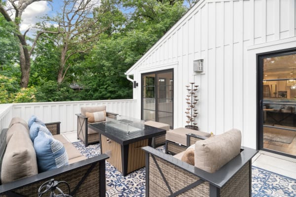 Outdoor balcony with wicker furniture, decorative plant, and green trees in the background.