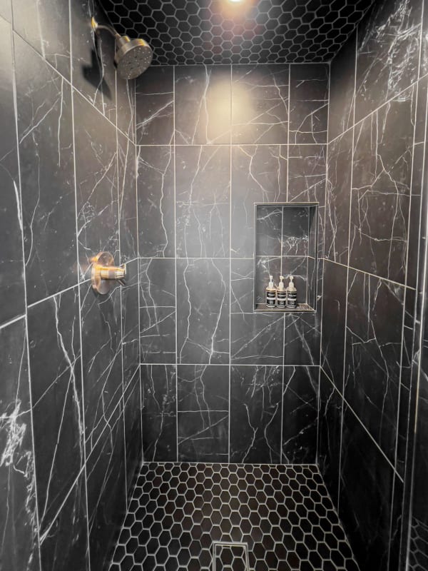Interior view of a luxury shower with dark marble tiles and hexagonal flooring.