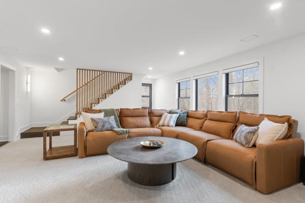 A comfortable living room featuring a large brown leather sofa, round marble coffee table, and staircase.