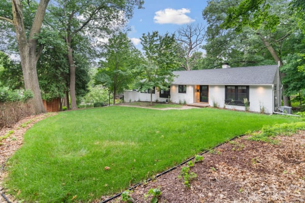 A modern house with a green lawn, trees, and a clear blue sky.