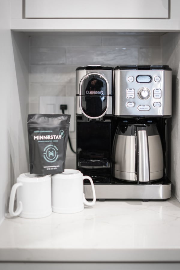 Modern Cuisinart coffee maker with coffee bags and white mugs on a marble countertop
