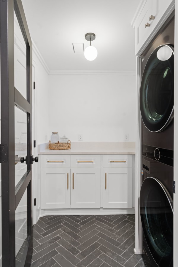Modern laundry room featuring dark herringbone tiles, white cabinetry, and black washer and dryer.