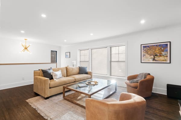 A contemporary living room featuring a tan sofa, glass coffee table, and artistic decor.