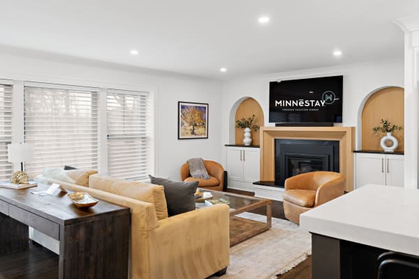 A contemporary living room with a beige sectional sofa, wooden desk, and a fireplace with a television above it.