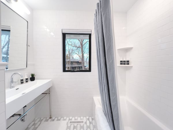 A minimalist bathroom with white subway tiles, a sleek bathtub, and a window showing outdoor trees.