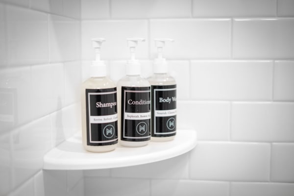Three personal care bottles on a shower shelf labeled shampoo, conditioner, and body wash.