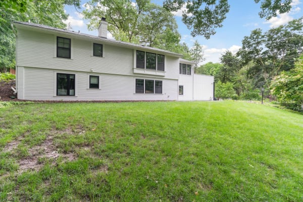 Exterior view of a modern two-story home with a sloping lawn and trees in the background.